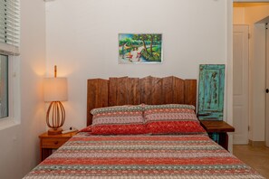 A bedroom with a wooden headboard, a patterned bedspread, a bedside lamp, a painting on the wall, and a rustic door. - High Life - Private Hilltop Estate With Pool And Panoramic Ocean 4 Bedroom Home (Governor's Harbour)