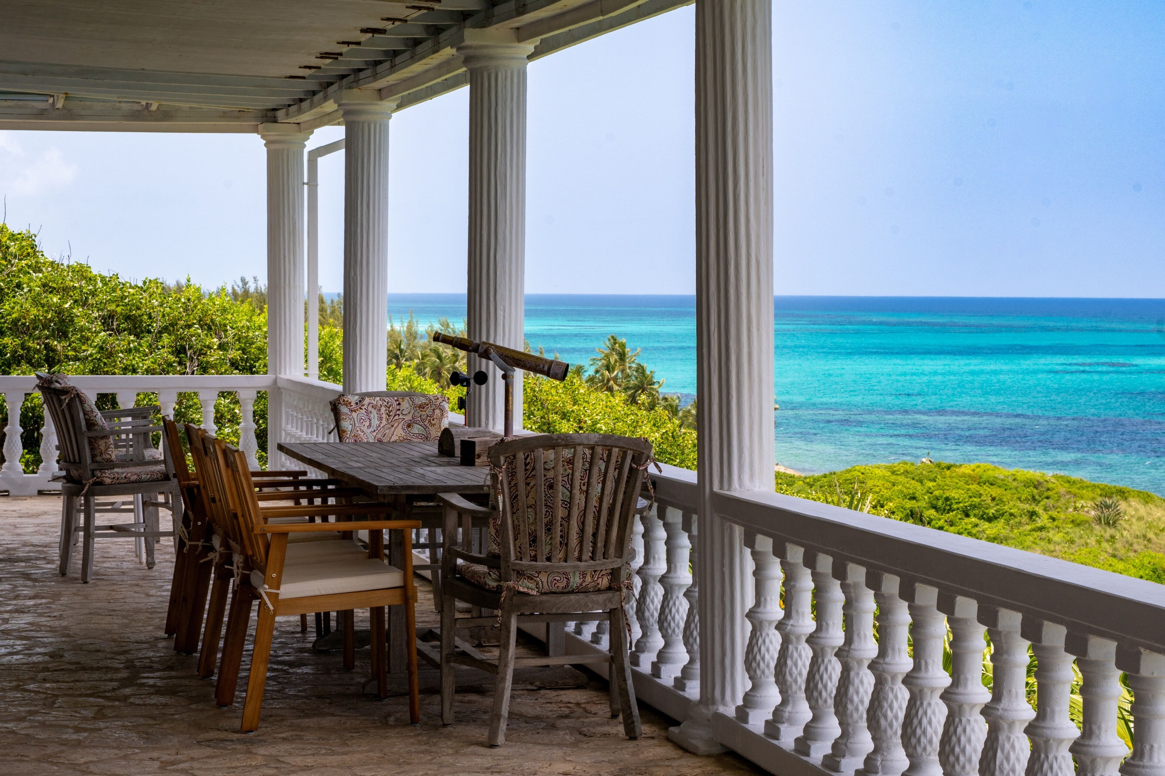 A covered outdoor seating area with a table and chairs, overlooking a turquoise sea.