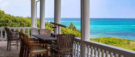 A covered outdoor seating area with a table and chairs, overlooking a turquoise sea.