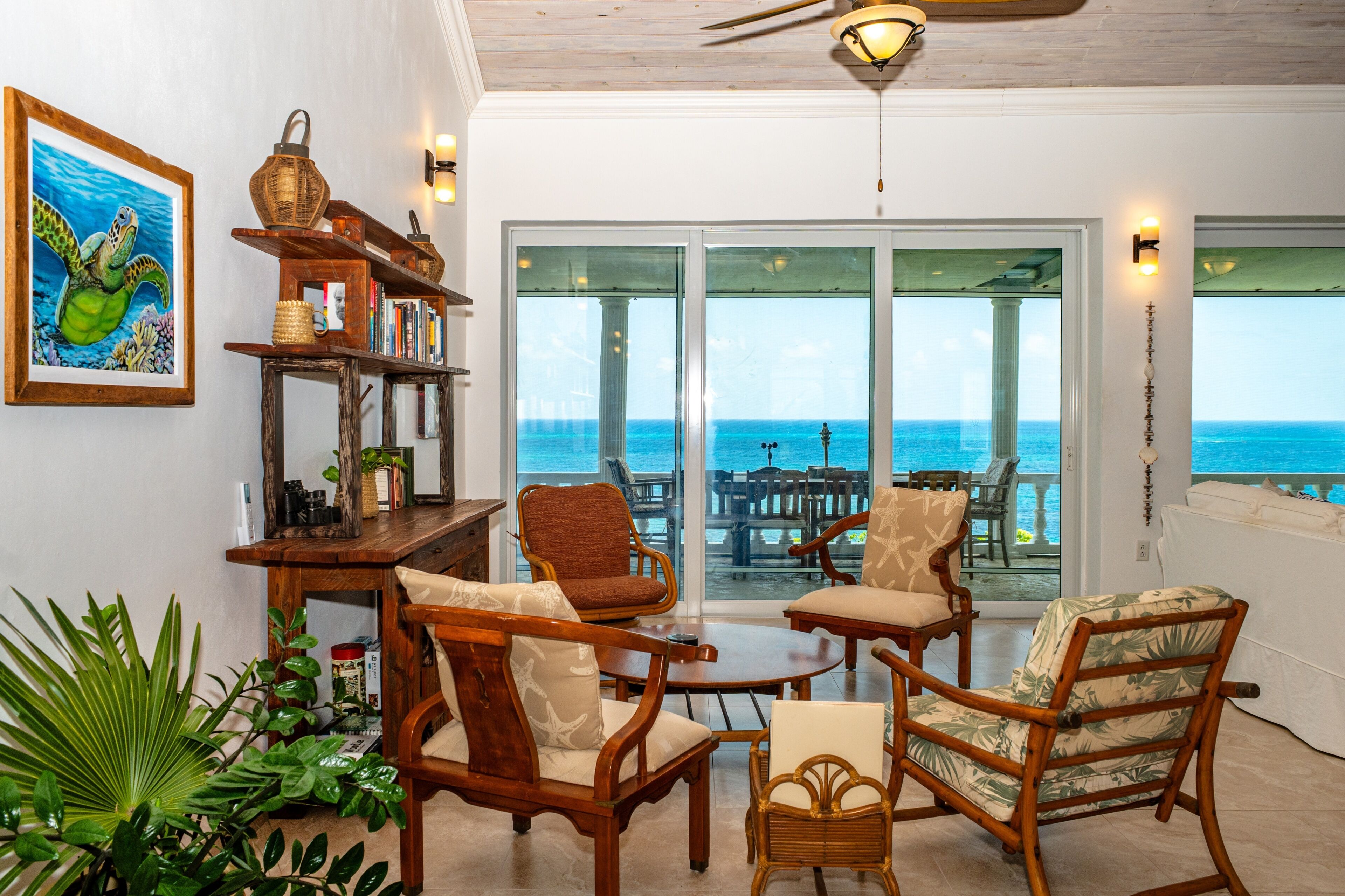 A room with a view of the ocean, featuring a wooden table, chairs, and a bookshelf.