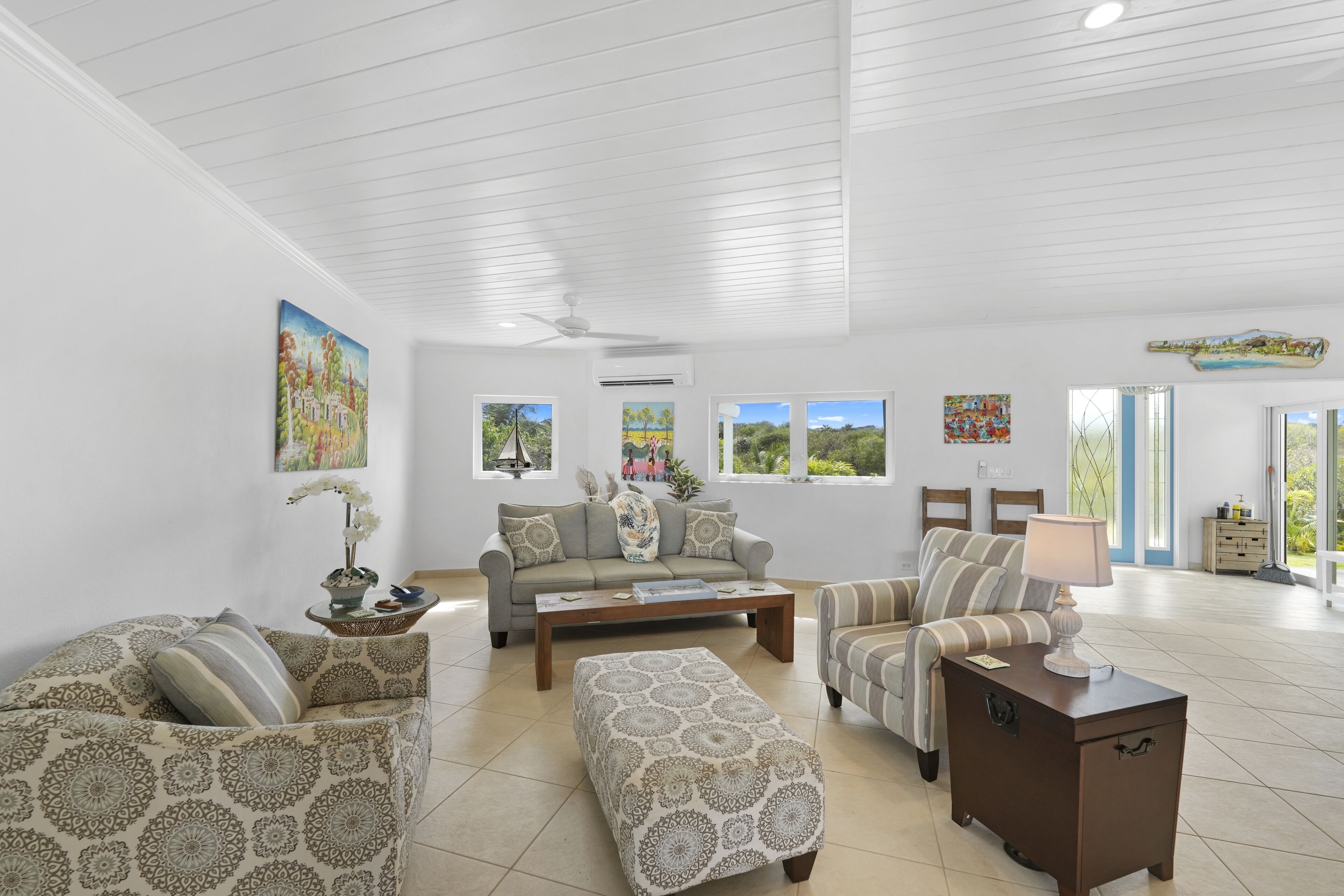 A spacious living room with a high ceiling, a sofa set, a coffee table, and artwork on the walls.