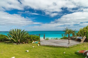 A wooden deck with a view of the ocean and a grassy area with plants. - Outer Reef - Newly Remodeled Beachfront House, Walk Rest/bar 2 Bedroom Home (Governor's Harbour)