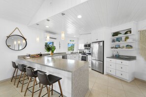 A modern kitchen with a central island, bar stools, white cabinetry, stainless steel appliances, and pendant lighting. - Outer Reef - Newly Remodeled Beachfront House, Walk Rest/bar 2 Bedroom Home (Governor's Harbour)