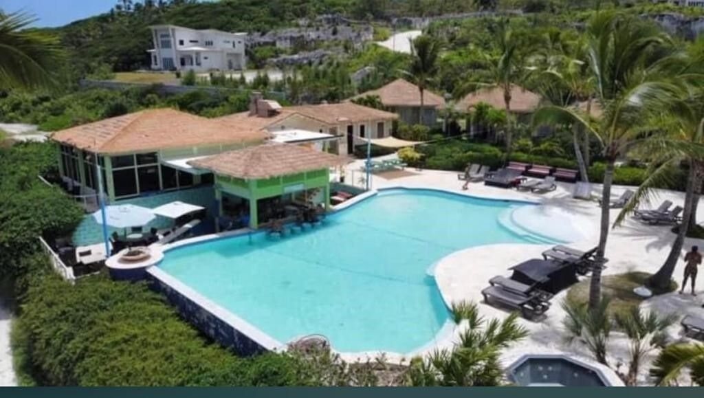 Ein Resort mit einem großen Schwimmbad, Liegebereichen und einem Gebäude mit einem Reetdach.