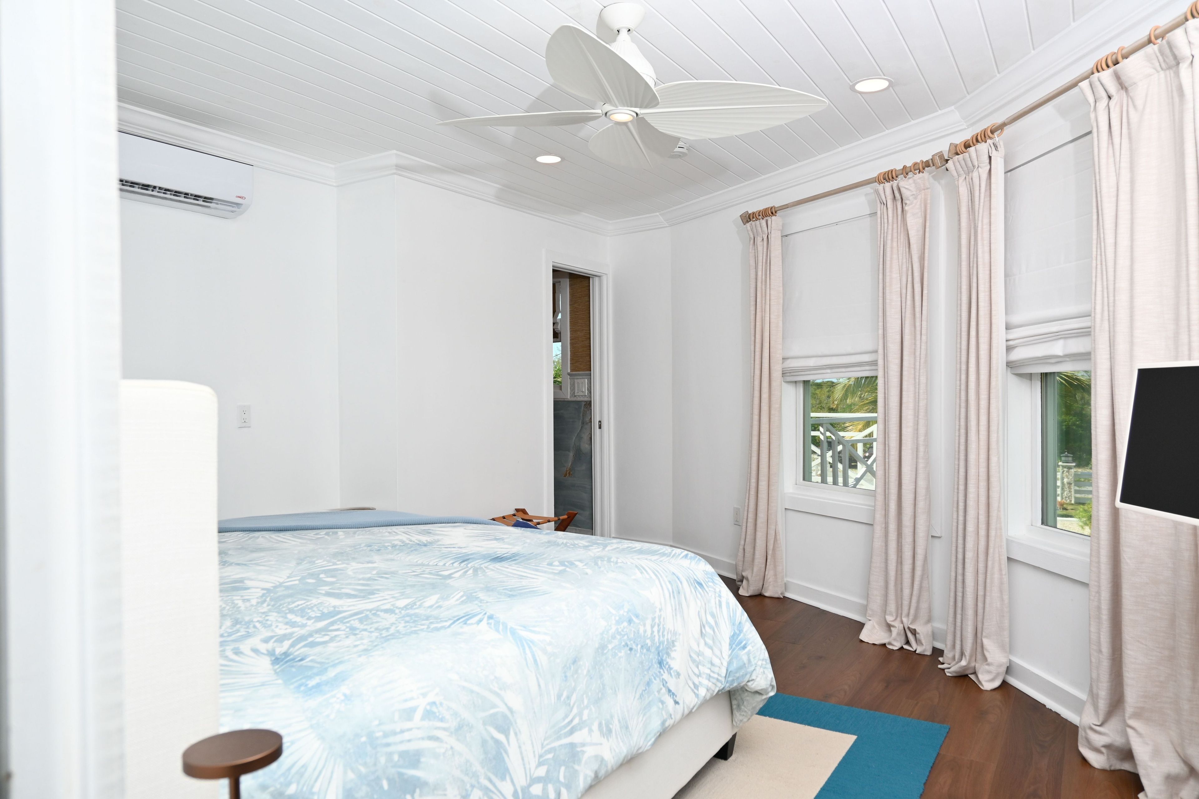 A bedroom with a bed, a ceiling fan, a window with curtains, and a view of the outdoors.