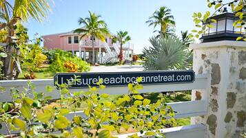 A sign with the text 'Laysurebeachcancaretreat.com' in front of a building with a white fence and greenery.