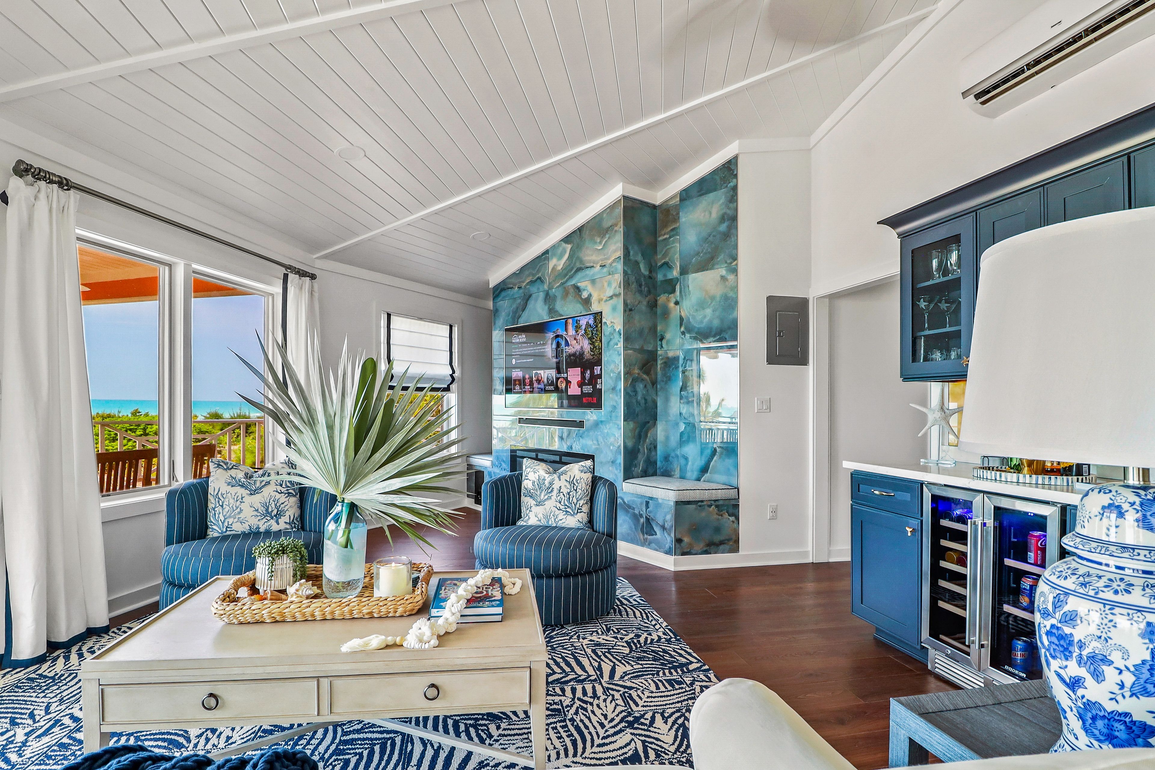A spacious living area with a large window, a sofa set, a coffee table, and a kitchen area with a wine fridge.