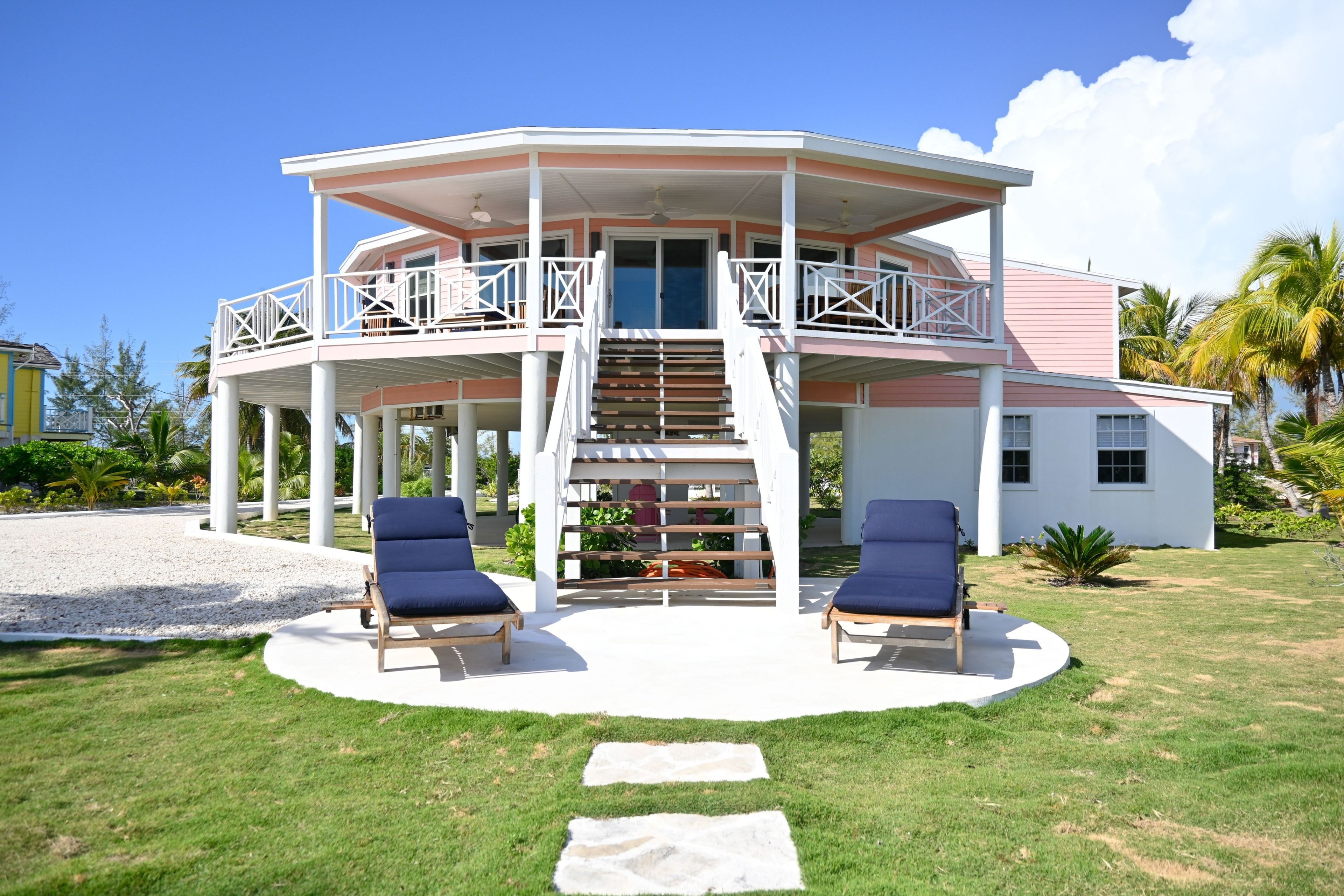 A two-story house with a covered patio, two lounge chairs, and a staircase leading to the upper level.