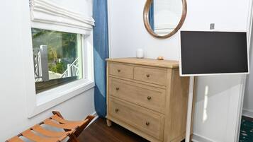 A room with a wooden dresser, a bench, a window with a view, a mirror, and a flat-screen TV.