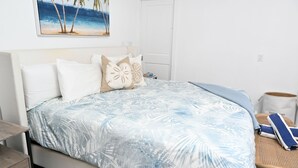A bedroom with a bed, pillows, a painting, a bedside table, and a chair. - Leisure Beach Ocean Retreat - Luxury Beachfront House 3 Bedroom Home (Current)