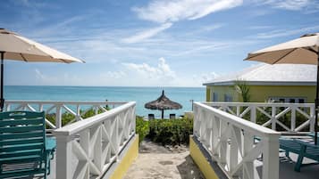 A pathway leading to a beach with umbrellas and chairs, a pool, and a view of the ocean.