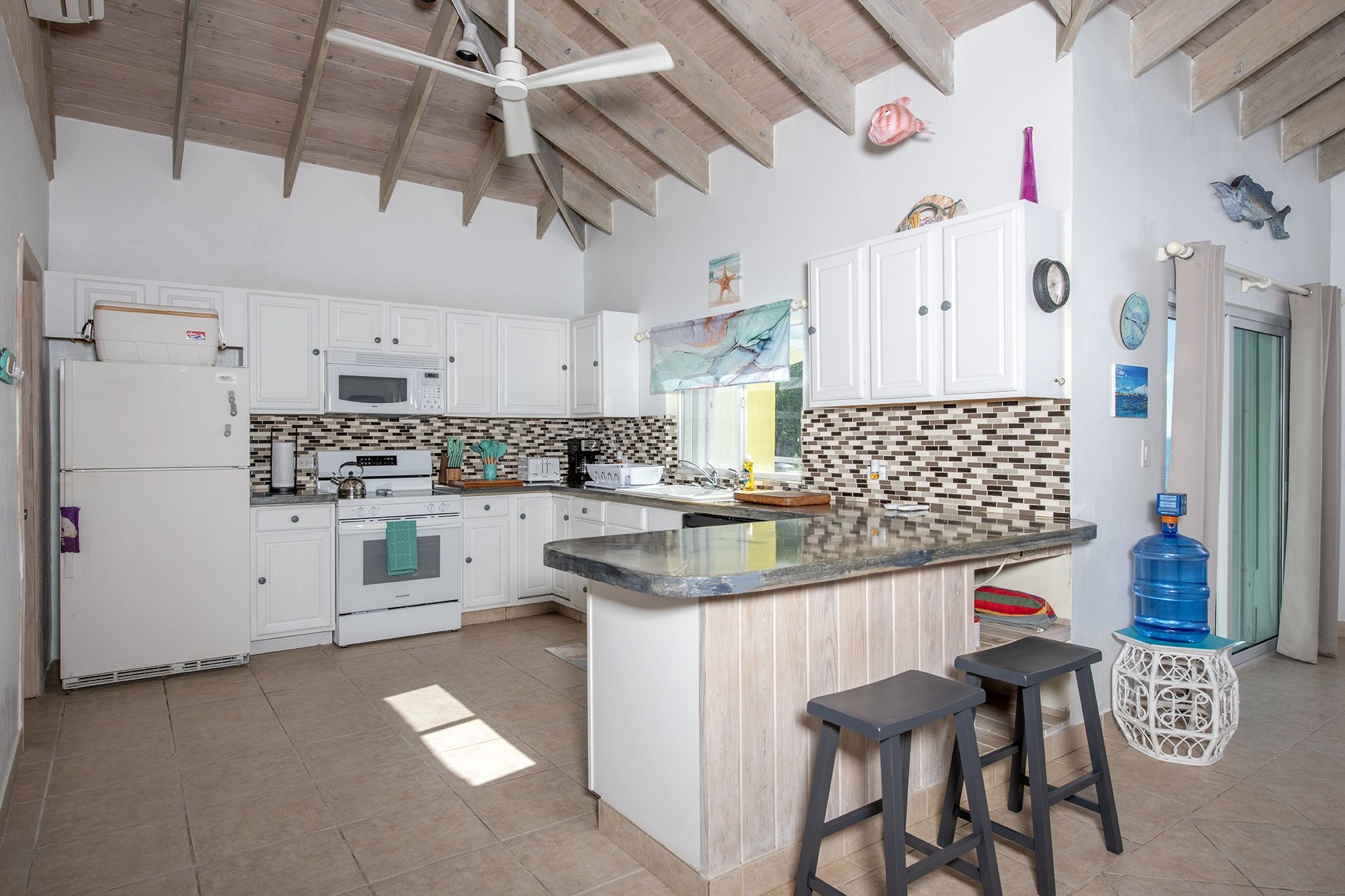 A kitchen with white cabinets, a central island, a microwave, a stove, and a ceiling fan.