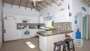 A kitchen with white cabinets, a central island, a microwave, a stove, and a ceiling fan.
