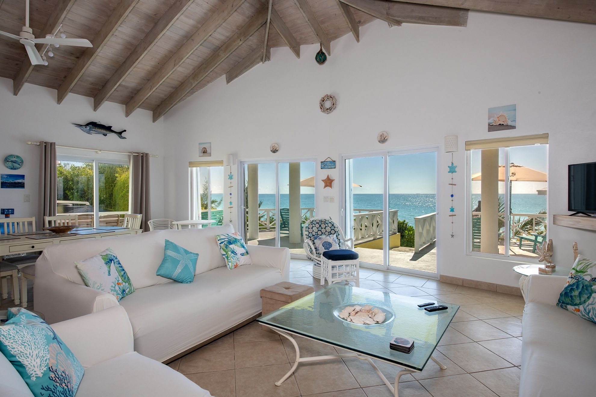 A spacious living area with a glass coffee table, white sofas, and a view of the sea.