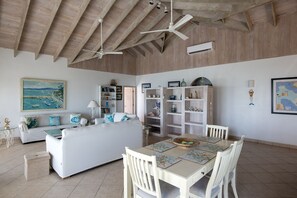 Un vaste espace de vie doté d’un haut plafond, d’un canapé blanc, d’une table à manger avec des chaises et d’une bibliothèque.