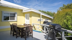 Eine Terrasse mit Tisch und Stühlen, einem Grill und einem Fenster mit Blick auf Grünflächen.