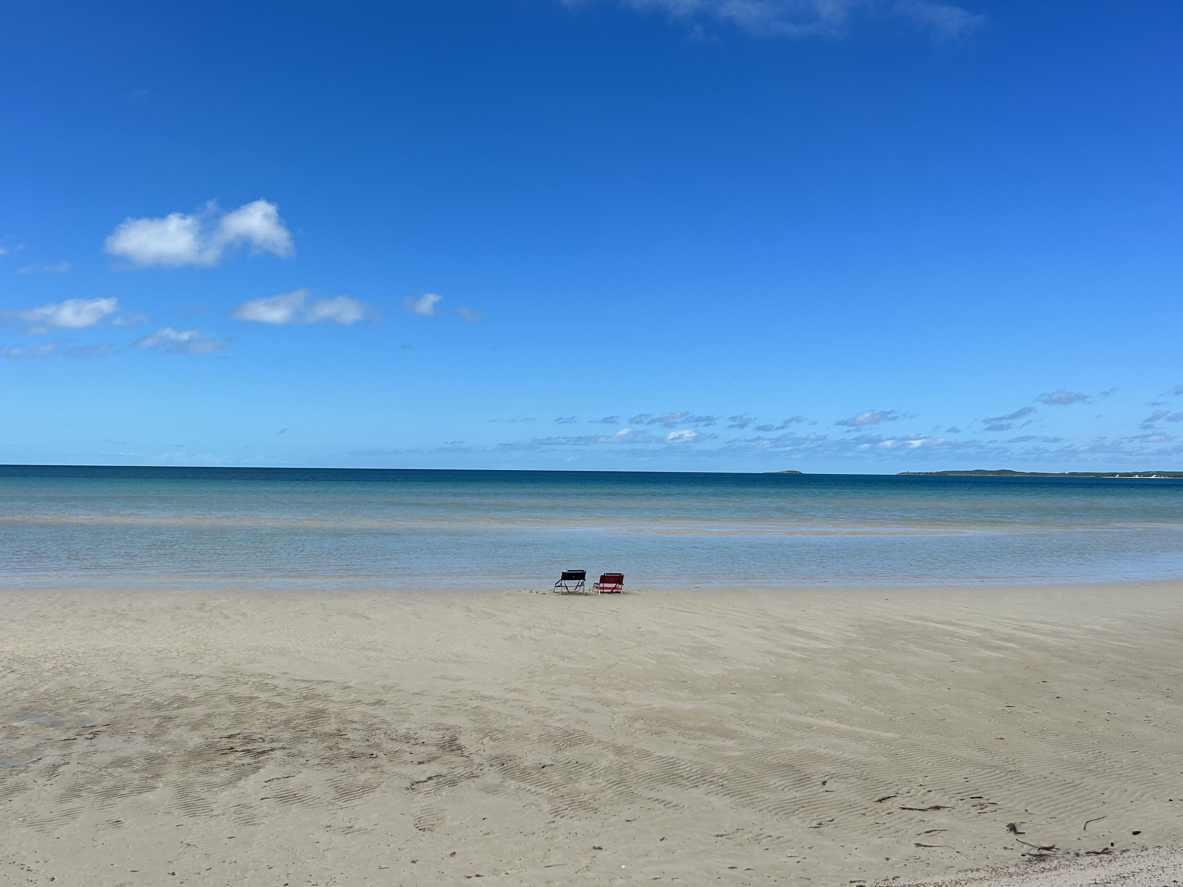 A beach with two chairs facing the ocean, clear skies, and calm water.