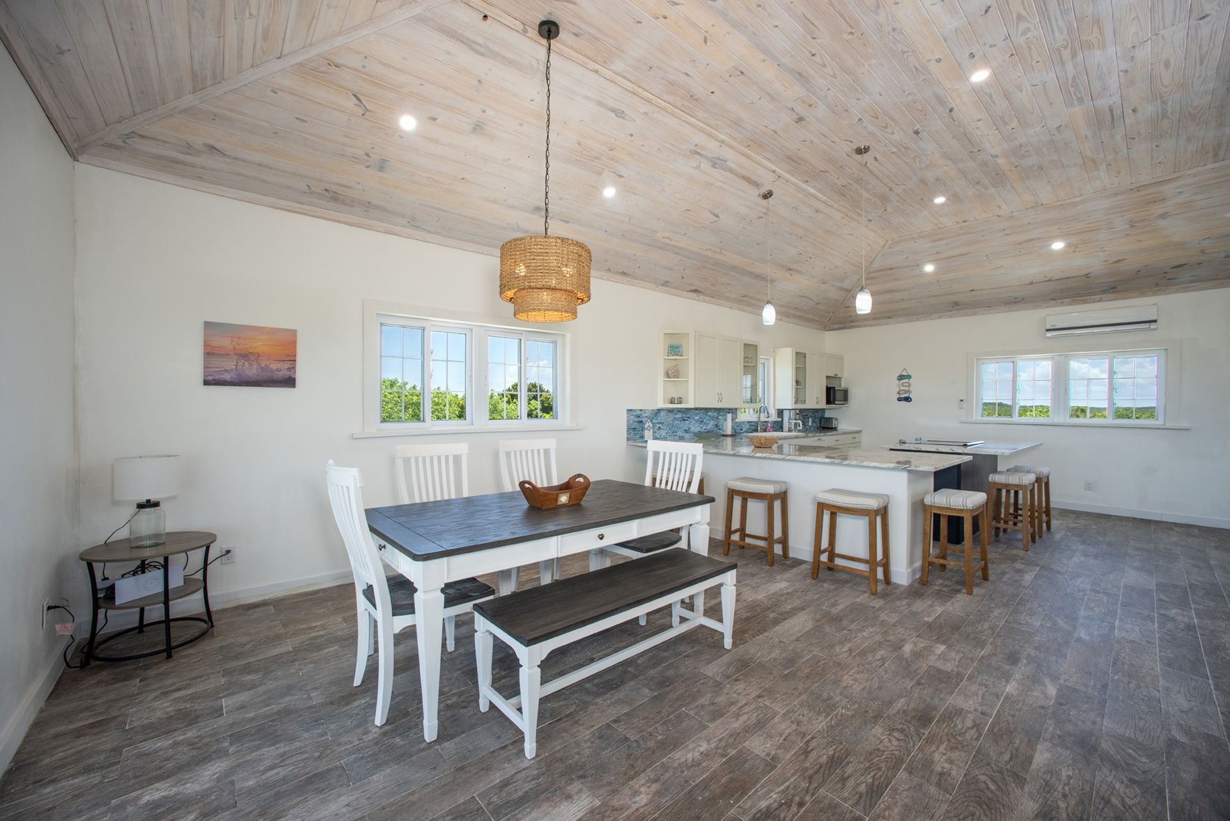 A spacious kitchen with a dining area, wooden ceiling, and large windows.