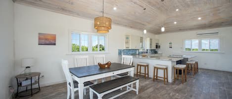 A spacious kitchen with a dining area, wooden ceiling, and large windows.