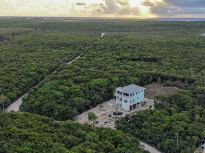 A two-story building with a flat roof and a balcony, surrounded by dense greenery. - Southern Comfort - Brand New Home Steps From Ten Bay Beach With 3 Bedroom Home (South Palmetto Point)