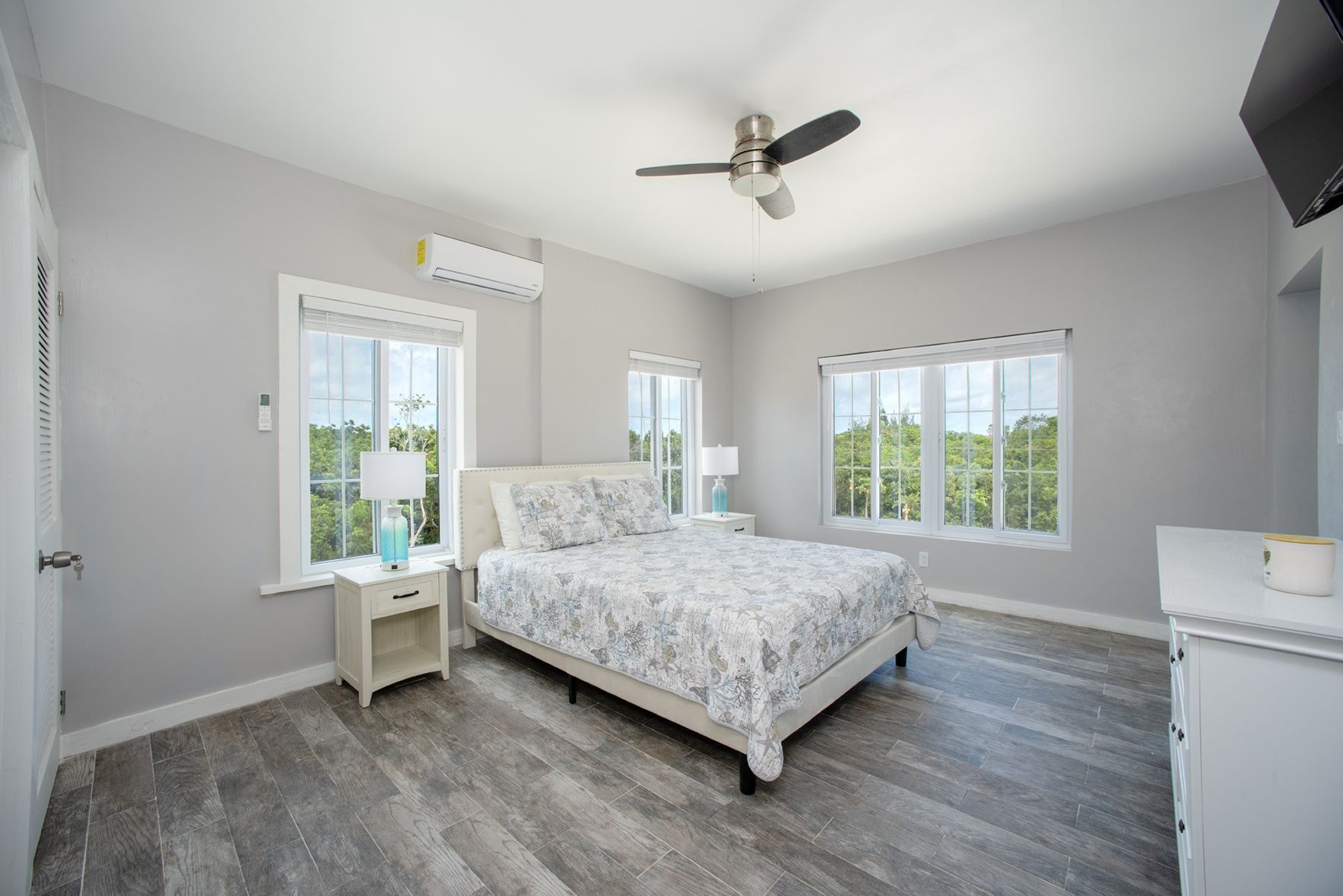 A bedroom with a bed, nightstands, a ceiling fan, and large windows.