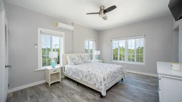 A bedroom with a bed, nightstands, a ceiling fan, and large windows.