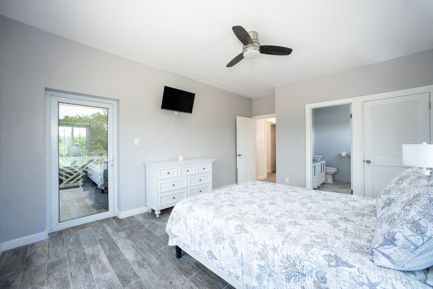 Een slaapkamer met een bed, een dressoir, een plafondventilator, een televisie en een badkamer die door een open deur zichtbaar is.