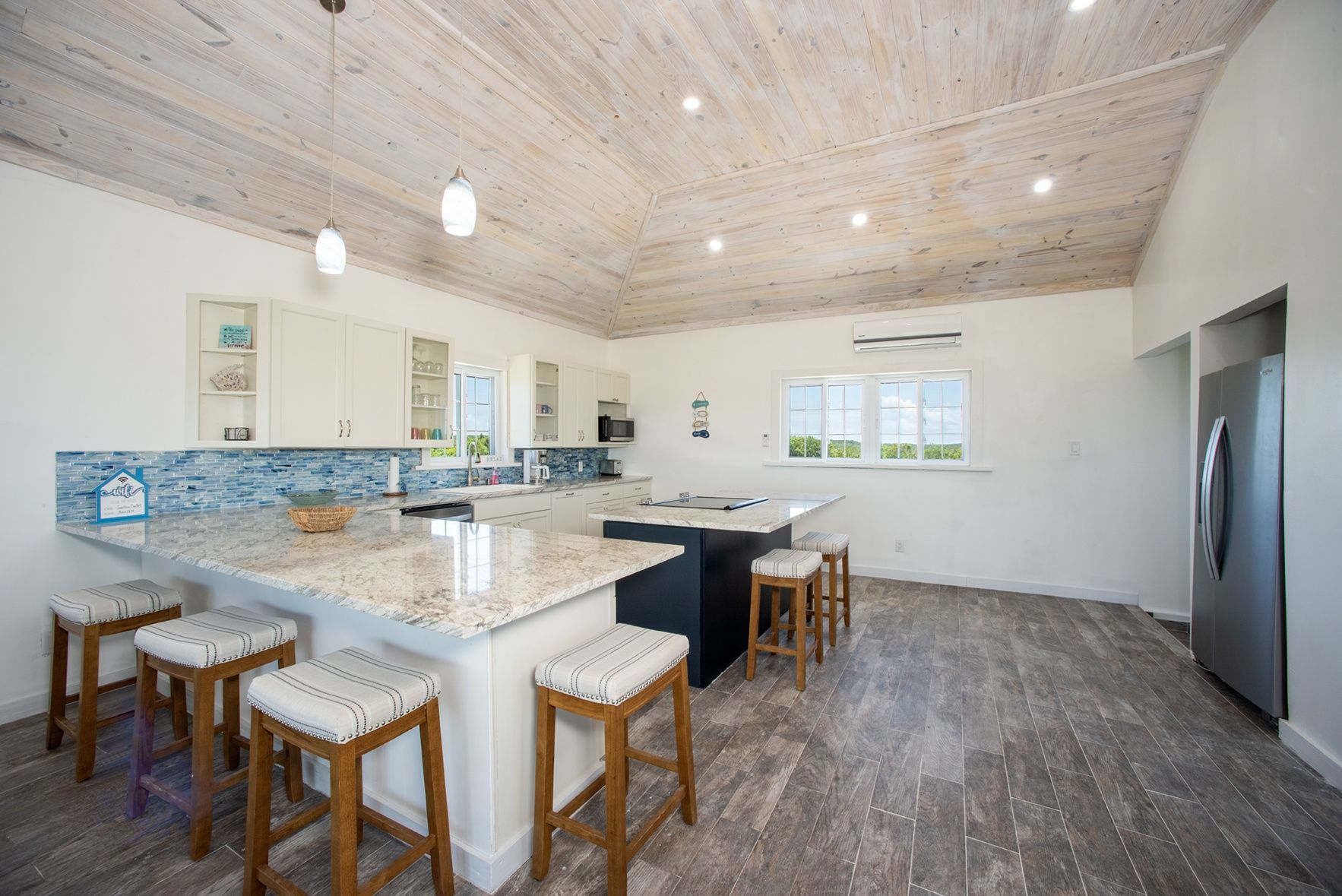 A modern kitchen with a large island, bar stools, and a refrigerator.