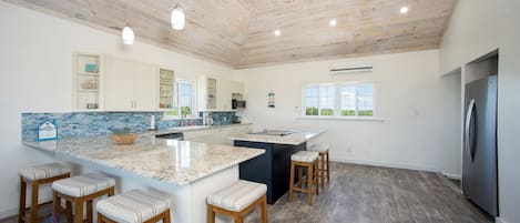 A modern kitchen with a large island, bar stools, and a refrigerator.