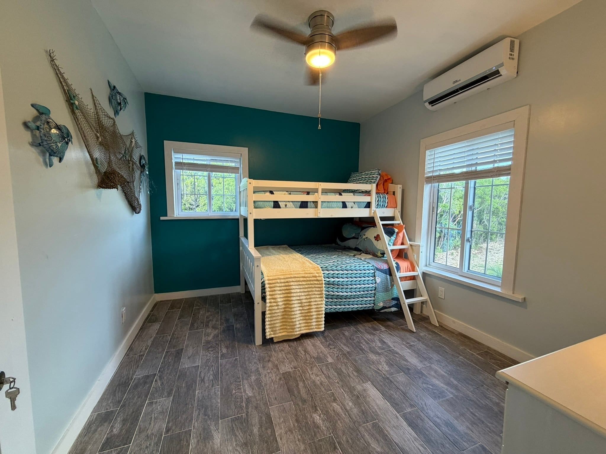 A child's bedroom with a bunk bed, two windows, a ceiling fan, and an air conditioning unit.