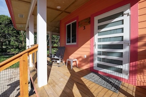 Eine Holzterrasse mit Geländer, einem Stuhl, einem kleinen Hocker und einer Tür mit Fenster.