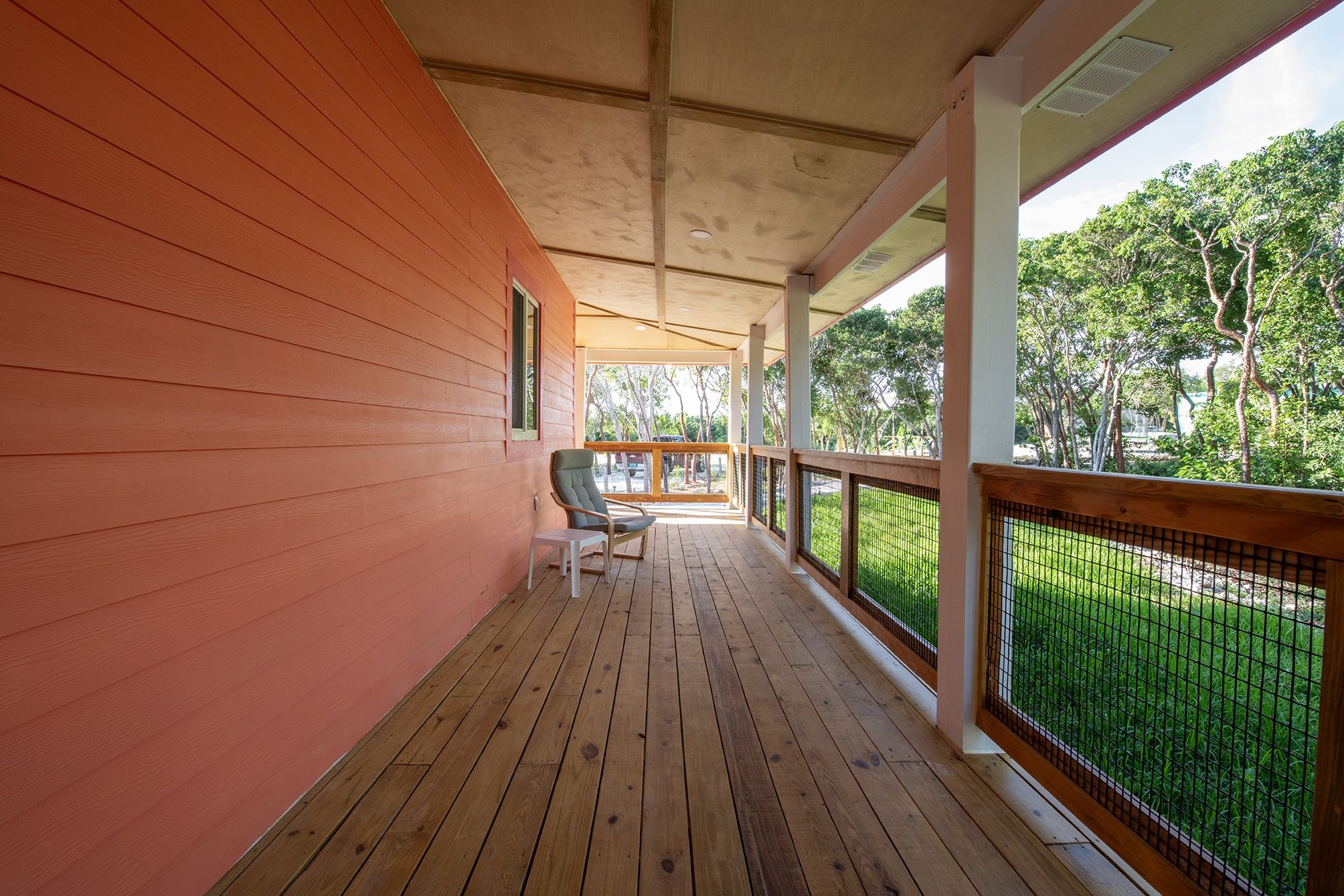 A covered porch with wooden flooring, a railing, and a view of greenery.