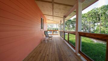 A covered porch with wooden flooring, a railing, and a view of greenery.