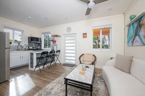 Eine moderne Küche mit Essbereich, ein Wohnzimmer mit Sofa und Blick auf Bäume durch die Fenster.
