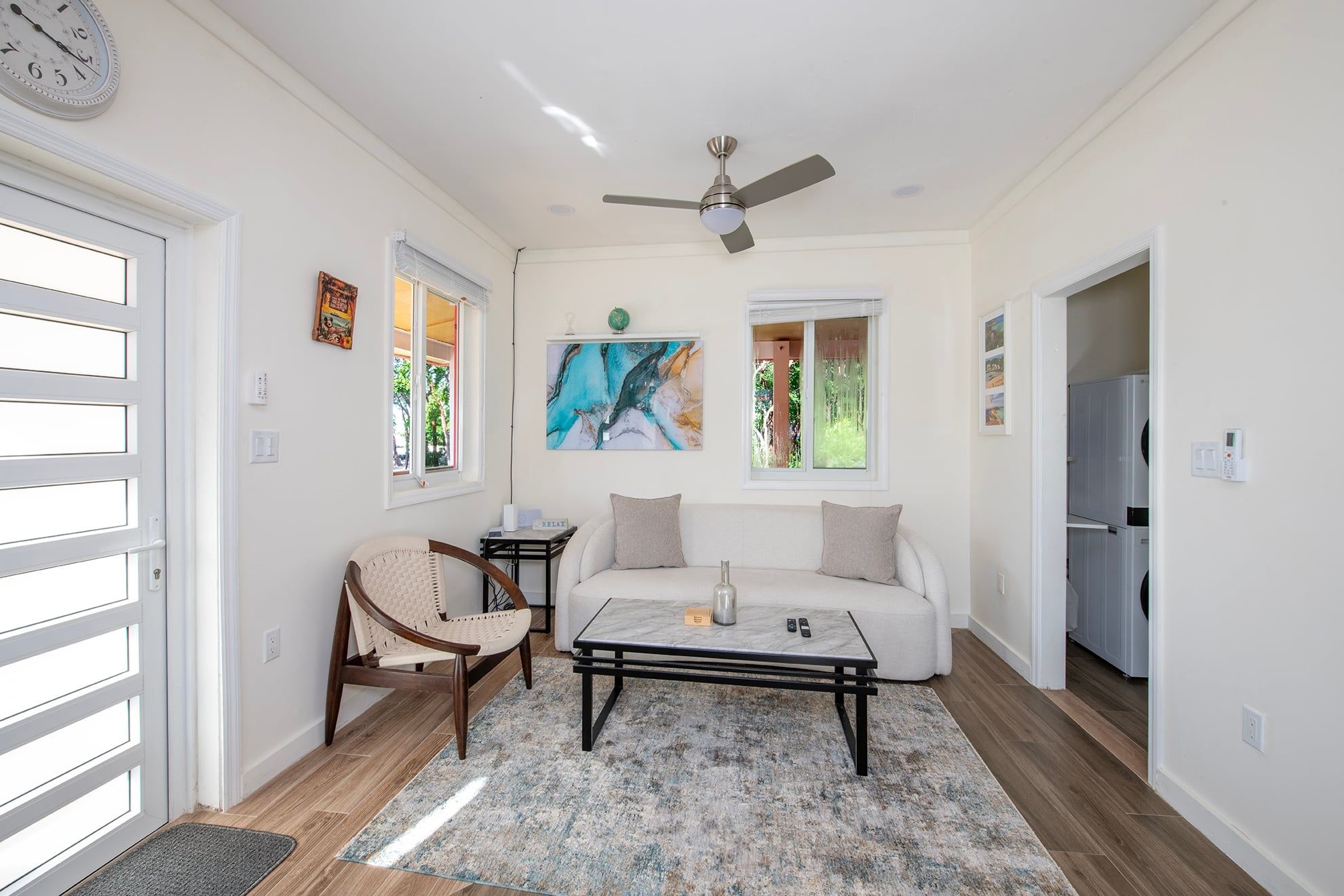 A living room with a sofa, a coffee table, a chair, a ceiling fan, and artwork on the wall.
