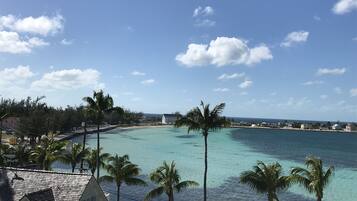 A coastal view with clear turquoise waters, palm trees, and a white building with a sloped roof.