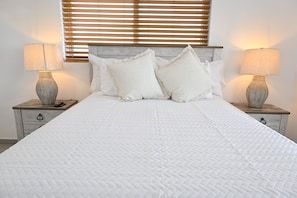 A bed with a white quilted bedspread, flanked by two nightstands with lamps and a vase on each. - Sapphire Cottage - Brand New Beach Villa With Pool 2 Bedroom Home (North Palmetto Point)
