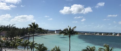 A coastal view with clear turquoise waters, palm trees, and a white building with a sloped roof.
