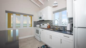 A modern kitchen with white cabinets, a black countertop, and a view of the ocean through large windows.