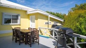 Ein gelbes Gebäude mit einem weißen Dach, einem Grill und einem Tisch mit Stühlen auf der Terrasse.