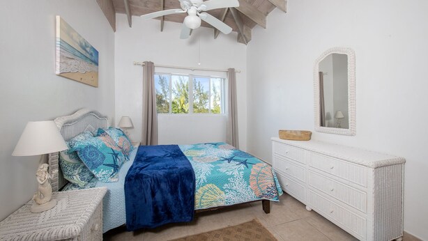 A bedroom with a bed, a nightstand, a dresser, a ceiling fan, and a window with curtains.