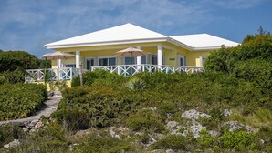A two-story building with a white roof and yellow walls, surrounded by dense greenery and a clear sky.