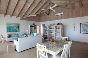 Un vaste espace de vie doté d’un haut plafond, d’une table à manger avec des chaises, d’un canapé avec des coussins et d’une bibliothèque.