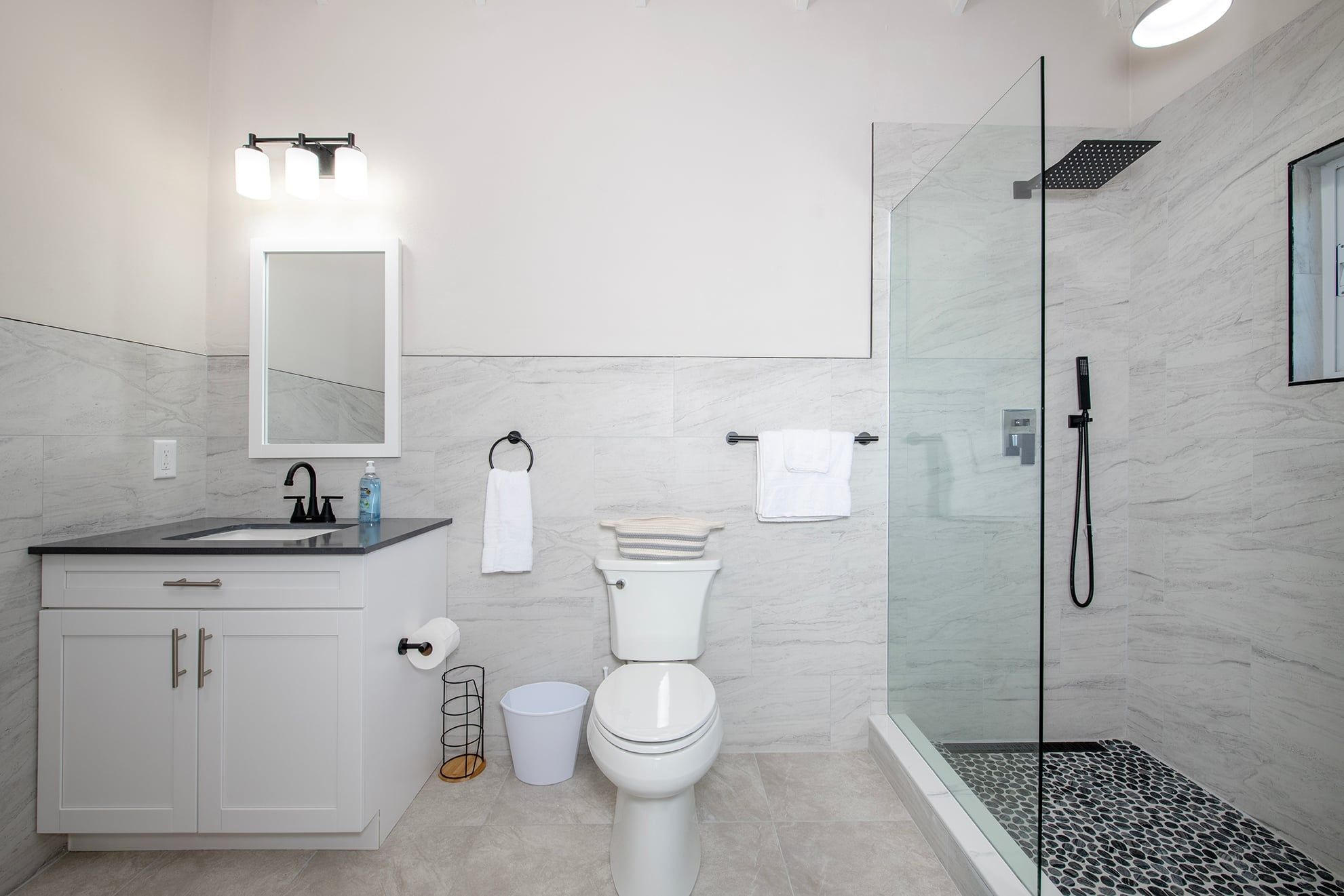 A modern bathroom with a glass-enclosed shower, a white toilet, a sink with a mirror, and a cabinet.