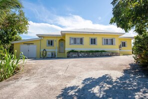 Un bâtiment jaune avec un garage, un mur en pierre et une allée pavée.