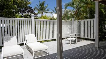 A covered outdoor area with a white fence, two white lounge chairs, and a small table.