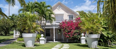 A two-story house with a balcony, surrounded by lush greenery and a well-maintained lawn.