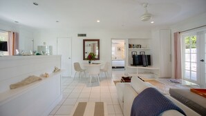 Uma sala de estar moderna com sofá, espaço de refeições com cadeiras, televisão e cozinha com bancada e armários.