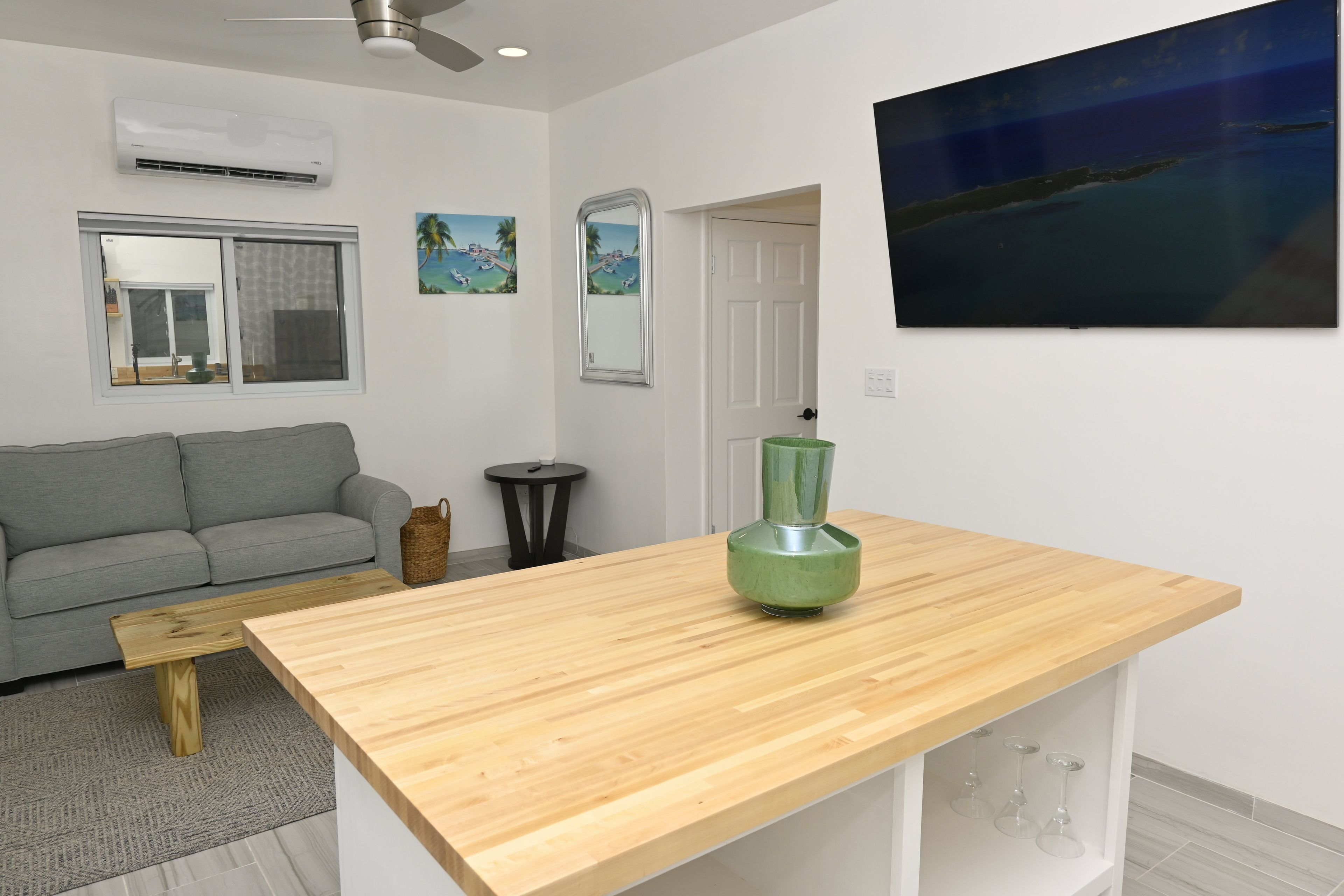 A modern living room with a grey sofa, a wooden coffee table, a green vase, and a painting of a tropical scene.