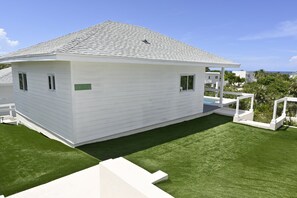 A white single-story house with a grey roof, a small front porch, and a well-maintained lawn. - Emerald Cottage - Brand New Beach Cottage With Pool, Walk To La 1 Bedroom Home (North Palmetto Point)